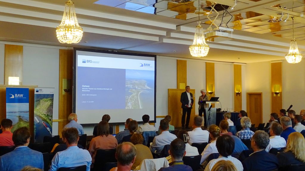 Foto der Begrüßung zum Ostsee-Kolloquium durch Holger Rahlf und Dr. Dorothe Herpertz vor der Titelfolie des Kolloquiums