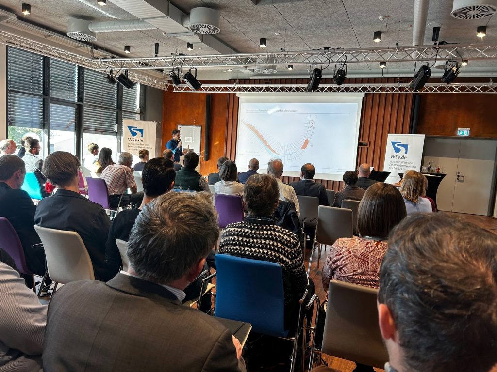 Das Bild zeigt K. Mouris beim Präsentieren des BAW-Beitrags. Im Vordergrund ist Publikum zu sehen.